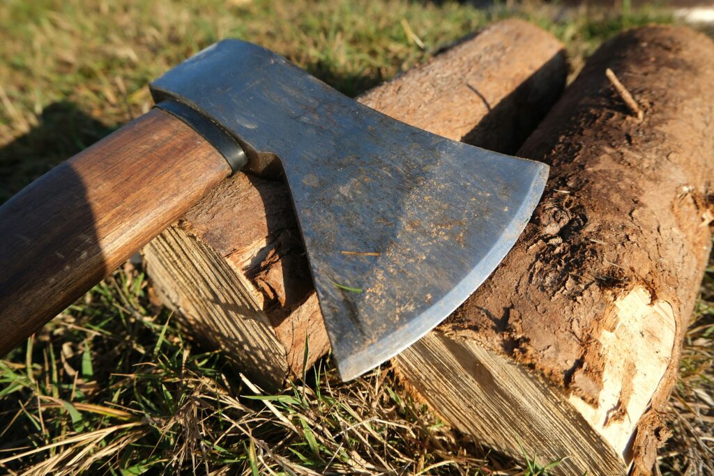 hacha para tallar madera apoyada sobre troncos en exterior
